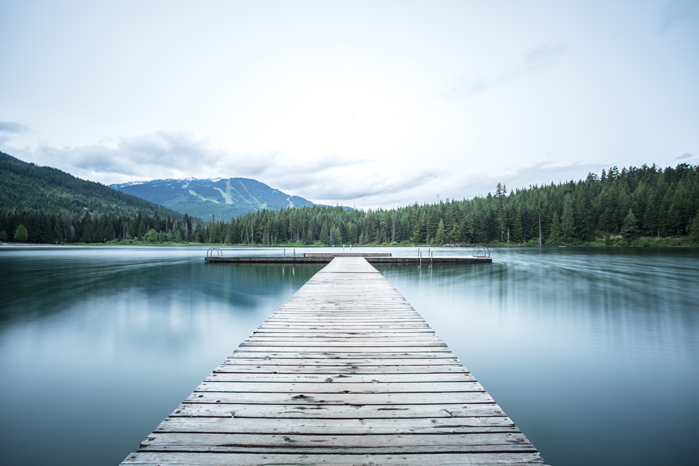 un ponton au bord d'un lac entouré de foret et montagnes