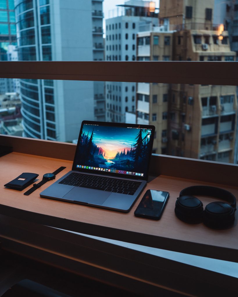 Bureau avec un ordinateur portable ouvert, un téléphone, un casque audio et une montre connectée, au bord d'une fenêtre menant sur la ville