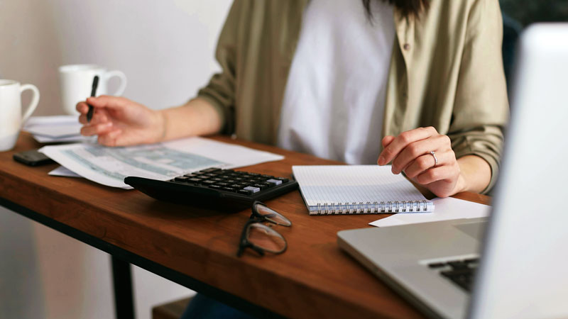 Personne faisant le bilan sur un bureau avec une tasse de café et un laptop ouvert